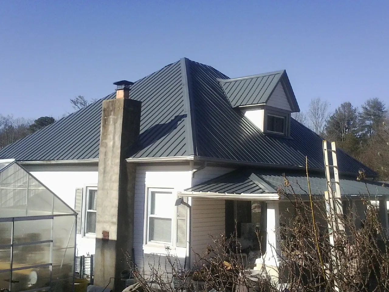 Dark blue standing seam metal roof on a white farmhouse with dormer — Slate & Tile Roof Repair by Roofing Brothers in Sheldahl