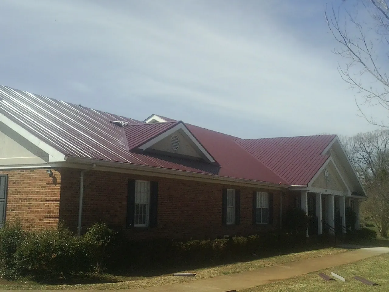 Red metal roof with gabled entries on a long brick building, from a Hail Damage Roof Repair job in Sheldahl