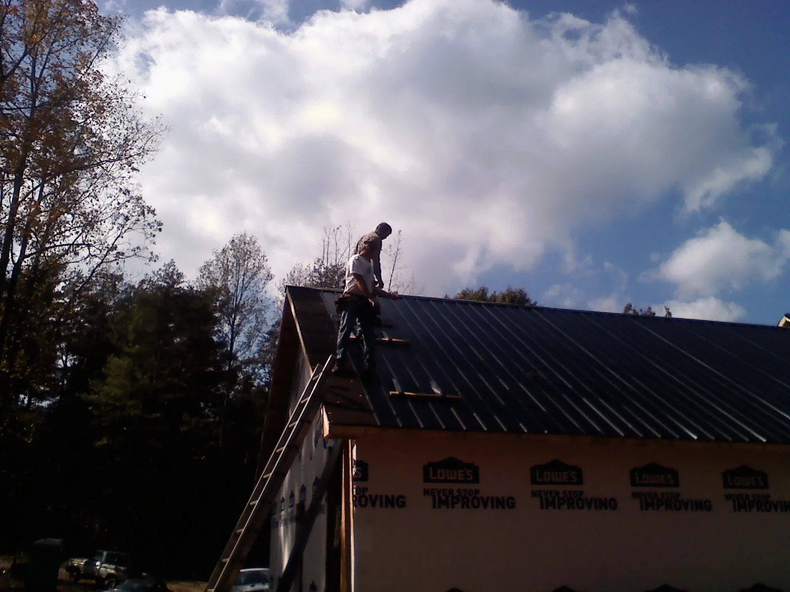 Roofer fastening dark metal panels high against a cloudy sky, from a Roof Inspection job in Sheldahl
