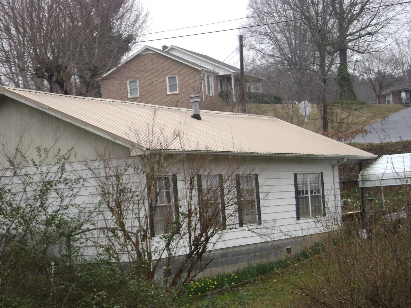Tan metal roof on a white sided house set into a hillside — Commercial Roofing by Roofing Brothers in Sheldahl