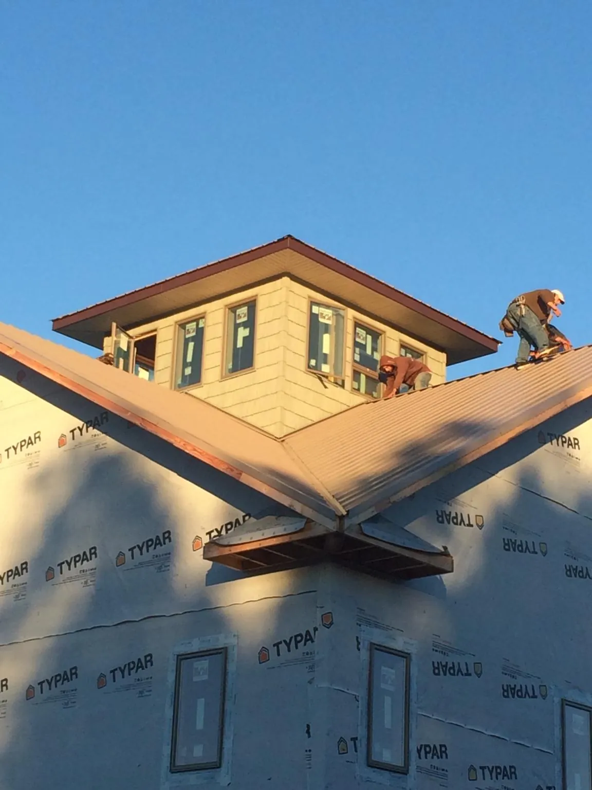 Roofers working around a rooftop cupola on a new metal roof at sunset — Roof Waterproofing in Sheldahl by Roofing Brothers